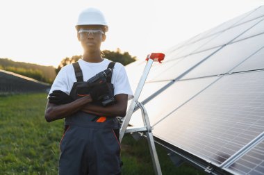 Genç adam güneş panellerinin yanında duruyor, sürdürülebilir enerji tesisi üzerinde çalışıyor. Yeşil teknolojiyi ve yenilenebilir enerjiyi destekliyorum.