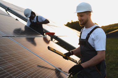 Güneş panellerini sürdürülebilir bir enerji çiftliğine kuran işçiler, gün batımında inşaat sırasında ölçüm ve ayarlama