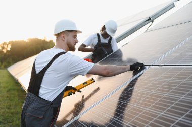 Güvenlik kaskı ve tulumu takan mühendisler güneş panellerini güneş çiftliğine yerleştiriyor ve temiz ve sürdürülebilir enerji üretiyorlar.