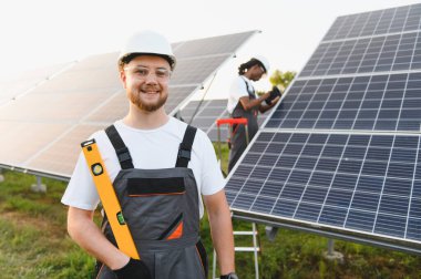 Bir güneş enerjisi santraline güneş panelleri kuran işçiler, temiz elektrik üretimini ve sürdürülebilir enerji gelişimini teşvik ediyorlar