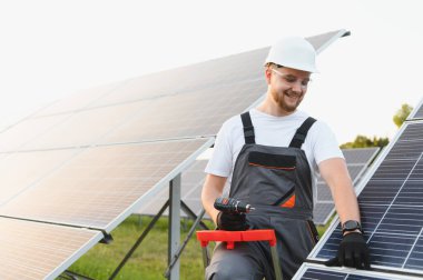 Sürdürülebilir enerji santrali inşaatı sırasında temiz enerji güneş panelleri kuran kasklı adam.
