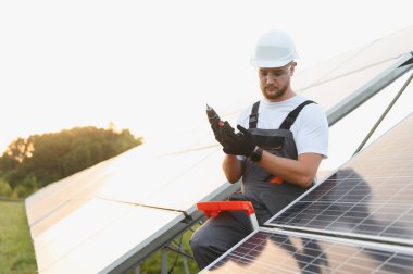 Profesyonel mühendis güvenlik donanımı takıyor ve temiz enerji için güneş panelleri kurarken matkabı ayarlıyor