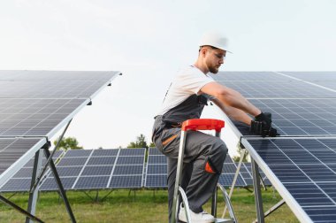 Sert şapka ve güvenlik gözlüğü takan işçiler yenilenebilir enerji santraline fotovoltaik paneller kuruyor.