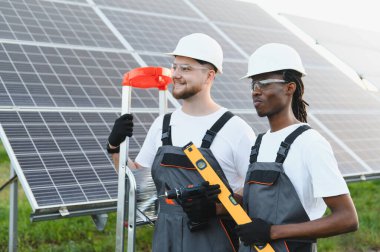 Bir güneş enerjisi santraline güneş panelleri kuran çeşitli işçiler temiz bir gelecek için sürdürülebilir yeşil enerji üretiyorlar.