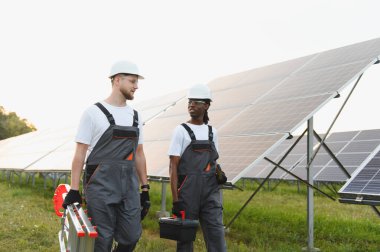Güneş çiftliğinde yürüyen iki mühendis, bakım için aletler ve merdiven taşıyorlar.