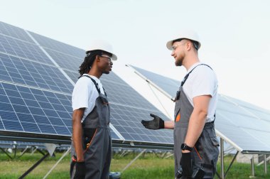 Güneş enerjisi çiftliğinde çalışan erkek mühendisler yenilenebilir enerji hakkında konuşuyor ve işbirliği yapıyorlar.
