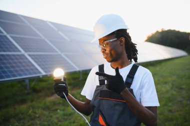 Afrikalı Amerikalı teknisyen elinde parlayan ampulü tutuyor, sürdürülebilir enerjiyi ve güneş enerjisinin yeniliğini simgeliyor.