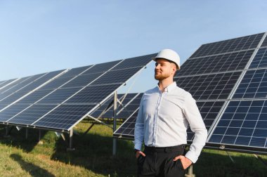 Sert şapkalı ve gömlekli bir adam büyük bir güneş panelinin önünde gururla duruyor, temiz enerjiyi ve sürdürülebilir geleceği temsil ediyor.