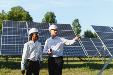 Bir güneş çiftliğinde iş birliği yapan mühendisler, planları gözden geçirir ve gün ışığında sürdürülebilir güneş enerjisi çözümleri planlarlar.