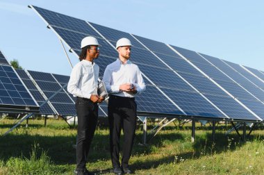 Sert şapkalı iki farklı mühendis bir güneş çiftliğinde yenilenebilir enerji geliştirme üzerinde çalışıyorlar.