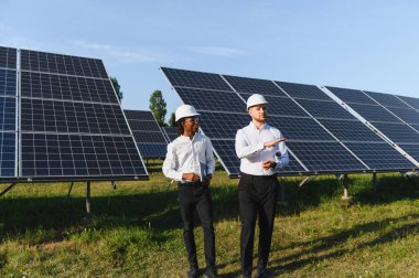 İki farklı mühendis bir güneş enerjisi santralinde operasyonları tartışıyor, takım çalışması ve sürdürülebilir enerji gelişimi.