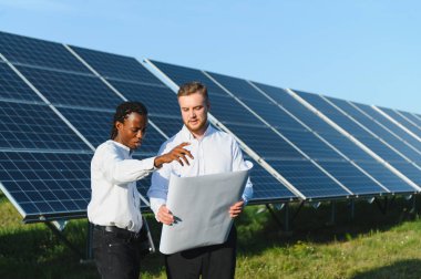 İki farklı mühendis bir güneş paneli çiftliğinde sürdürülebilir enerji çözümleri planlayan bir planı tartışıyor.