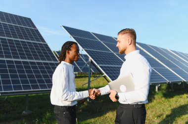 İki farklı işadamı güneş panelleri yakınında el sıkışıyor, ortaklığı sembolize ediyor, yenilenebilir enerji ve sürdürülebilir iş geliştirme