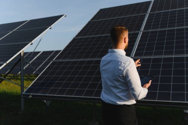 Bir fotovoltaik enerji santrali üzerindeki güneş panellerini inceleyen mühendis, temiz enerji üretimi ve sürdürülebilir teknoloji sağlıyor.