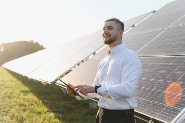 Genç adam güneş panellerini uzaktan izlemek için dijital tablet kullanıyor. Sürdürülebilir enerji ve yeşil teknoloji kavramı