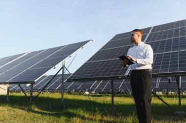 Genç adam dijital tablet kullanarak güneş enerjisi performansını analiz ediyor, temiz enerji ve sürdürülebilirliği teşvik ediyor.