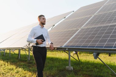 Erkek mühendis tablet tutuyor, güneş panellerini inceliyor, sürdürülebilir yeşil enerji çözeltisi projesi üzerinde çalışıyor