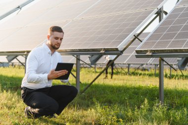 Güneş enerjisi santralini denetleyen resmi kıyafetli bir adam veri analizi ve sürdürülebilir enerji yönetimi için bir tablet tutuyor.