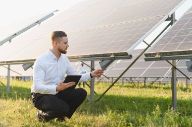 Enerji çiftliğindeki güneş panellerini kontrol eden mühendis veri analizi ve yenilenebilir enerji yönetimi için bir tablet tutuyor.