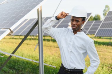 Genç siyah mühendis veya işçi güneş panelleri arasında güvenle duruyor, yenilenebilir enerji ve sürdürülebilir teknolojiyi destekliyor