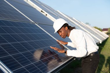 Güneş fotovoltaik panellerini denetleyen, yenilenebilir enerji sisteminin işlevselliğini ve sürdürülebilirliğini sağlayan bir başlık içindeki Afrikalı Amerikalı mühendis.