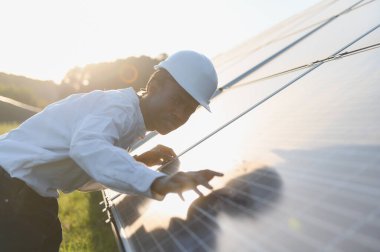 Genç erkek mühendis güneş panelini incelerken başlık takıyor. Yenilenebilir temiz enerji ve sürdürülebilir güç üzerine odaklanılıyor