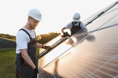 Büyük bir alana fotovoltaik güneş panelleri kuran işçiler, günbatımı ışığı ile sürdürülebilir temiz enerji üretiyorlar.