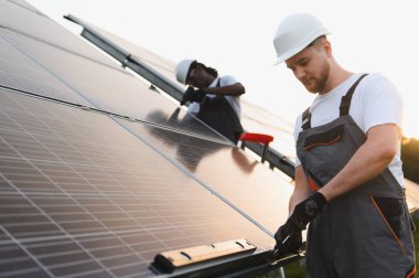 Çeşitli işçiler fotovoltaik güneş panelleri kuruyor, sürdürülebilir elektrik üretimine ve temiz geleceğe katkıda bulunuyor