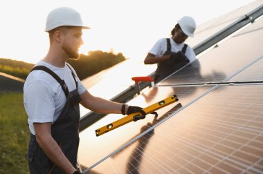 Sert şapka ve tulum giyen mühendisler bir güneş kurulum alanı üzerinde çalışarak güç üretimi için verimlilik ve sürdürülebilirlik sağlıyorlar.