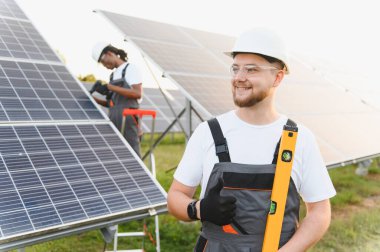 Başka bir işçi ekipman yerleştirirken, gülümseyen teknisyen güneş panelleri önünde başparmak kaldırıyor.