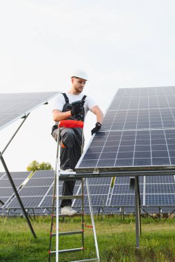 Merdiven üzerinde çalışan bir işçi güneş paneli kuruyor. Yenilenebilir enerji, sürdürülebilirlik ve yeşil güç kavramları