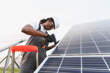 Afrikalı Amerikalı adam güneş panelleri kuruyor, sürdürülebilir elektrik üretimini sağlıyor ve yenilenebilir enerjiye katkıda bulunuyor