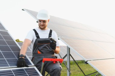 Yenilenebilir enerji istasyonuna güneş panelleri kuran bir adam. Elektrikli bir alet kullanan yeşil teknoloji işçisi
