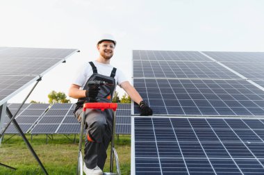 Bir güneş paneli sisteminin parçalarını birbirine bağlayan merdivendeki işçiler, sürdürülebilir enerji için temiz yenilenebilir enerji üretiyor