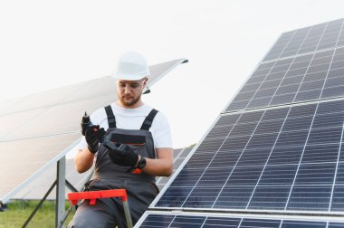 Baret takan ve koruyucu gözlüklü genç bir adam güneş enerjisi çiftliğinde çalışırken matkap hazırlıyor.