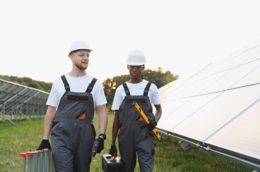Alet ve merdiven taşıyan iki farklı mühendis, sürdürülebilir bir enerji santralinde büyük bir güneş paneli dizisi üzerinde çalışıyorlar.