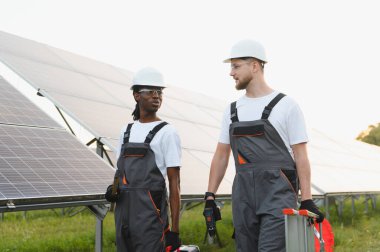 Güneş panellerinin yeşil bir alanda kurulumu ve bakımı hakkında konuşan iki farklı teknisyen.