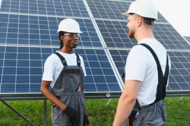 Bir güneş enerjisi santrali kurulumu üzerinde çalışırken yenilenebilir enerji ve sürdürülebilirliği tartışan iki farklı mühendis.