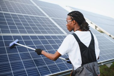 Geniş bir güneş panelini temizleyen genç adam yenilenebilir enerji üretimi için bakım yapıyor.