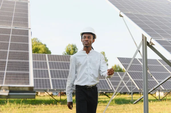 Güneş çiftliğinde yürürken kasketli genç adam fotovoltaik teknolojiyi değerlendiriyor ve temiz enerji üretiyor.