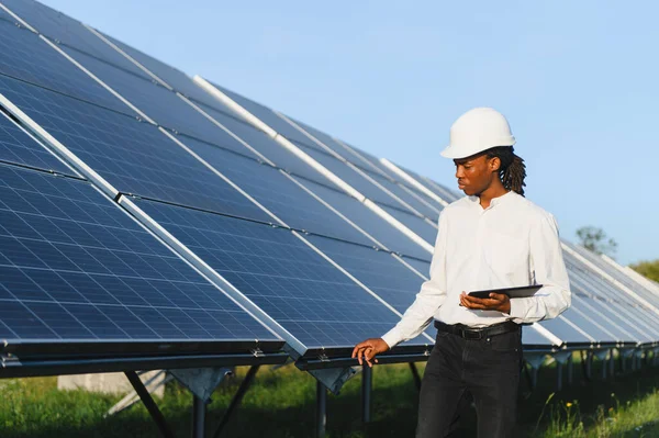 Başlık takan ve elinde dijital tablet bulunan genç adam, sürdürülebilir enerji üreten fotovoltaik panelleri kontrol ediyor.