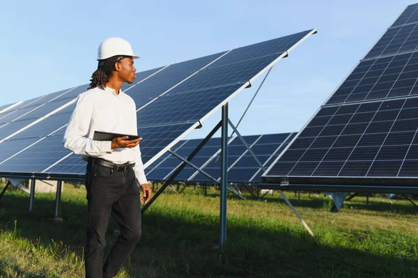 Elinde tablet olan Afrika kökenli Amerikalı mühendis güneşli bir alandaki güneş panellerini kontrol ederek yenilenebilir enerji üretimini sağlıyordu.