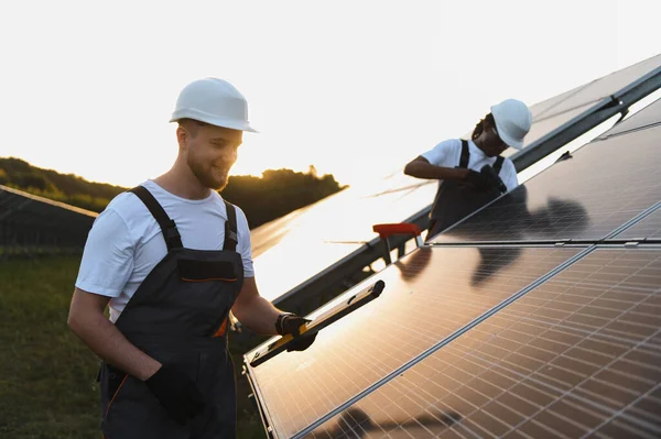 Bir güneş enerjisi santraline fotovoltaik paneller kuran işçiler, günbatımında sürdürülebilir enerji ve yenilenebilir enerji uzmanlığı sağlıyorlar
