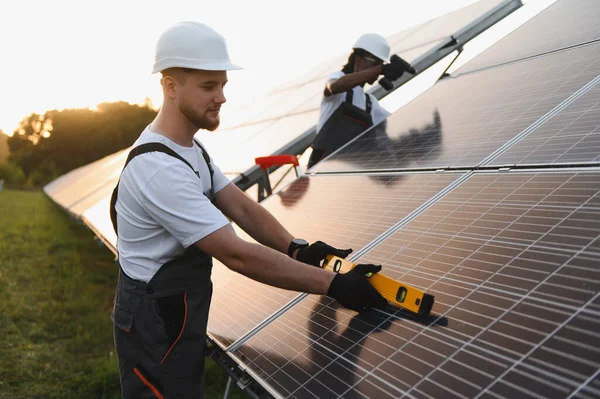 Teknisyenler sabit başlık ve güvenlik teçhizatı takıyor. Sürdürülebilir elektrik gücü için fotovoltaik sistemleri kontrol edip kuruyorlar.