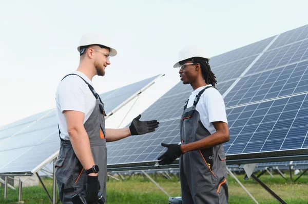 Çeşitli mühendisler, yenilenebilir enerji çözümleri ve sürdürülebilir enerji üretimini tartışarak, güneş paneli kurulumunda işbirliği yapıyorlar.