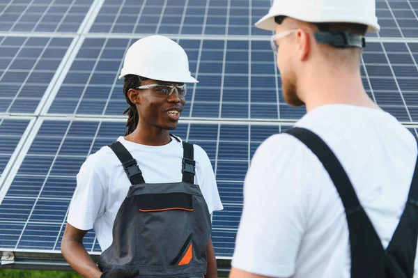 İki mühendis, güneş enerjisi santralinde, panellerin önünde çalışmaktan bahsediyorlar.