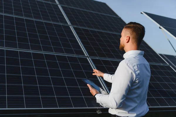 Güneş çiftliğindeki fotovoltaik panelleri gözlemleyen mühendis, yeşil enerji teknolojisinin veri analizi ve bakımı için bir tablet tutuyor.