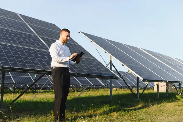 Bir güneş çiftliğinde çalışan mühendis yenilenebilir enerji üretimi ve sürdürülebilirliği için dijital tablet üzerindeki verileri analiz ediyor.