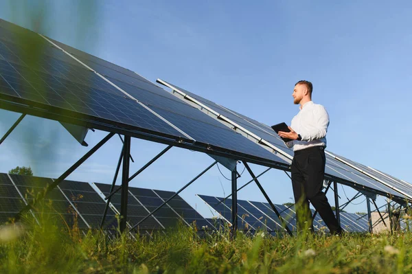 Dijital tablet tutan, güneş panelleri arasında yürüyen, verimli yenilenebilir enerji üretimi sağlayan adam