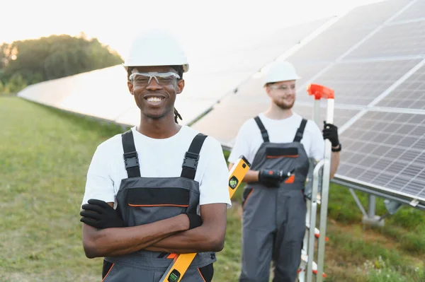Çeşitli mühendisler, yeşil enerjiyi, takım çalışmasını ve yenilenebilir elektrik üretimini sembolize ederek bir güneş enerjisi santraline gülümsüyor.